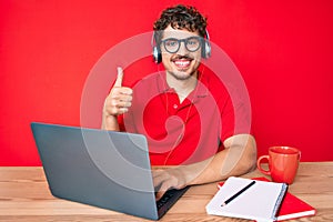 Young caucasian man with curly hair working at the office drinking a cup of coffee smiling happy and positive, thumb up doing