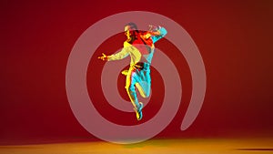 Young Caucasian man dancing hip-hop isolated over red background in neon light