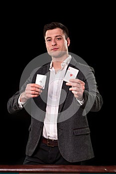 Young caucasian man wearing suit holding two aces in his hands on black background. Gambling concept. Casino