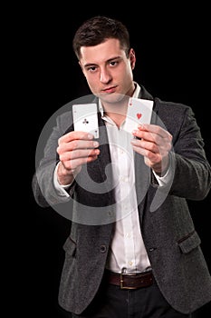 Young caucasian man wearing suit holding two aces in his hands on black background. Gambling concept. Casino