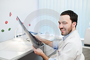 Young caucasian man doctor examines MRI image of human head in office looking at the patient and smiling