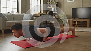 Young caucasian man doing floor push-ups at home in living room
