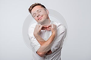 Young caucasian man doing a heart gesture against a white background