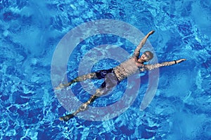 Young caucasian man floating on blue water in swimming pool. Top view. Summer vacation, relaxation, tourist on vacation