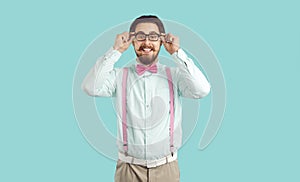 Young Caucasian man with funny beard and moustache smiling adjusts glasses, stands in studio