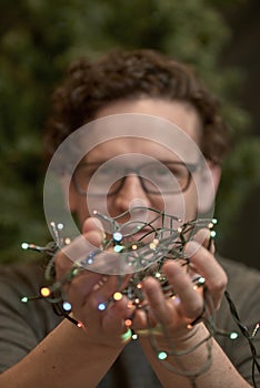 Young man holding a string of colored Christmas lights in both hands