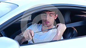 Young Caucasian man in glasses sitting on car with an open window while fastening seat belt Transport, safety and