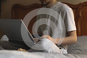 A young caucasian man holds a bank card in his hand and type on the keyboard of a laptop