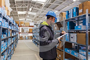 Young caucasian man in helmet, worker in warehouse checking carton boxes goods. Stock of Parcels with Products, transportation