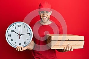 Young caucasian man holding delivery package and clock smiling and laughing hard out loud because funny crazy joke