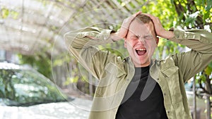 Young caucasian man holding his hands behind his head and screaming outdoors.