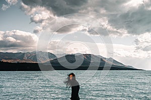 young caucasian man with long disheveled hair wearing t-shirt and black pants looking at camera from rough sea by