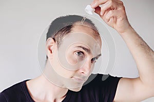 Young caucasian man looking at mirror and applying anti-hair loss concentrate serum