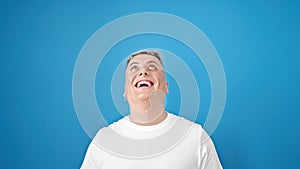 Young caucasian man looking up with surprise expression over isolated blue background