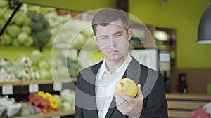 Young Caucasian man looking at yellow pear in grocery and showing thumb up. Confident guy choosing fruits for healthful