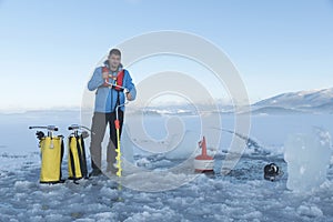 Young Caucasian man making hole in a frozen lake for ice diving.