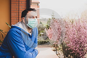 Young caucasian man with mask looking out onto home terrace during quarantine due to coronavirus covid19 pandemic