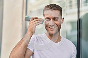 Young caucasian man miling confident listening audio message by the smartphone at street