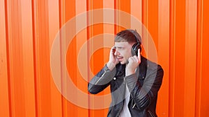 Young caucasian man in music headphones listens to music and dances on orange background, prance, slow motion, earpieces