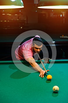 Young caucasian man playing billiard in club.