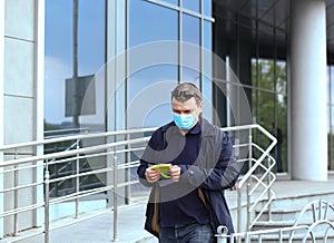 A young Caucasian man in a protective mask and black glasses stands near a car, bought a new green protective mask for a woman.