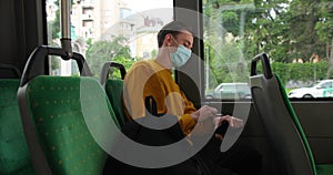 Young caucasian man rides a bus with medical mask on face. Sad guy with allergy looking at road through window. Virus