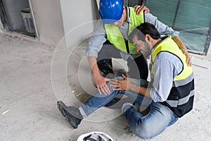 Young caucasian man in safety vest gripped his knee and screams in pain. Due to injuries at the construction site. His asian