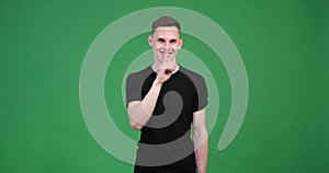 Young caucasian man showing shh gesture on green background