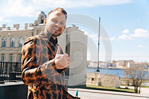 A young Caucasian man shows a claas finger up against a beautiful backdrop of houses. The concept of a successful businessman in a