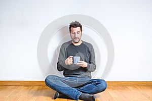 Young caucasian man sitting on the floor with a mug on his hands