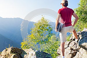 Young caucasian man sitting outdoor on a rock working on a laptop pc in mountain area.