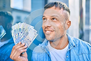 Young caucasian man smiling happy holding south african rands banknotes standing at the city photo