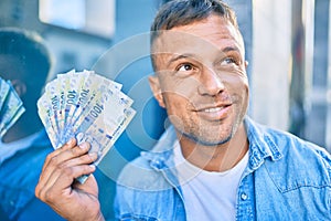 Young caucasian man smiling happy holding south african rands banknotes standing at the city photo