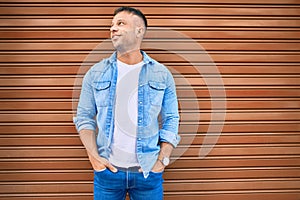 Young caucasian man smiling happy leaning on the wall at the city