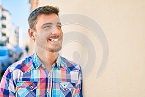 Young caucasian man smiling happy leaning on the wall at the city