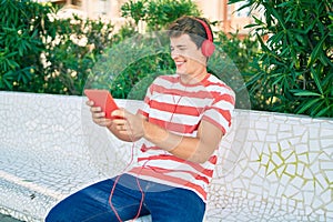 Young caucasian man smiling happy using touchpad and headphones sitting on the bench
