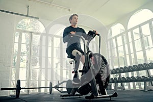 Young caucasian man in sports clothing cycling with prosthetic leg on exercise bike at the gym