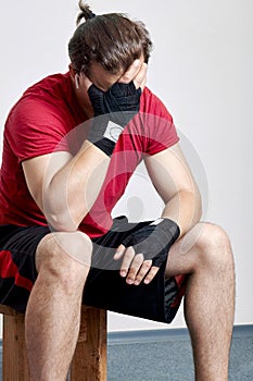 Young caucasian man in sportswear and boxing bandages sits with palm face. Despair moment, sorrow, hopelessness, despond before or