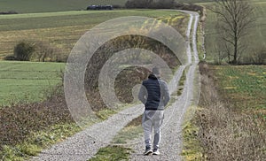 Young Caucasian man in sportswear walking along a path winding through green and yellow grasses.