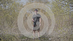 Young Caucasian man standing with fishing rod in spring forest. Wide shot portrait of fisherman waiting for fish to