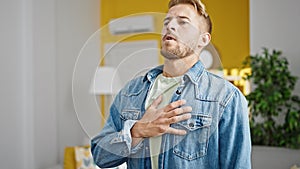 Young caucasian man standing with hand on heart listening to anthem at home