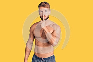 Young caucasian man standing shirtless asking to be quiet with finger on lips