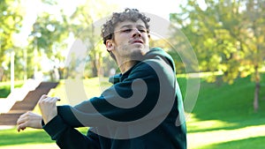 Young Caucasian man stretching before outdoor activities. Guy feeling pain in his neck standing in green park on sunny