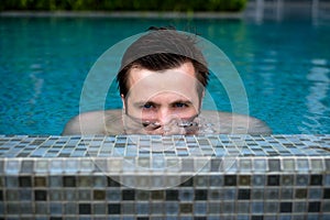 Young caucasian man swimming and lurking on summer vacation at pool. Half head above water stalking.