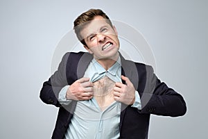 Young caucasian man tearing his shirt in anger