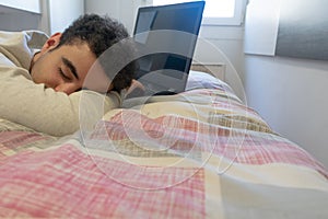 Young caucasian man tired in front of his laptop, sleeping on his bed