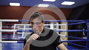 Young caucasian man training on boxing ring in modern gym. Fighting the shadow. Kickboxer in black T shirt and long hair