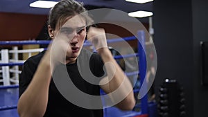 Young caucasian man training on boxing ring in modern gym. Fighting the shadow. Kickboxer in black T shirt and long hair