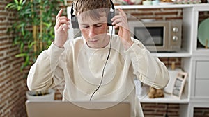 Young caucasian man using laptop and headphones at dinning room