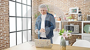 Young caucasian man using laptop and headphones holding cup of coffee at dinning room